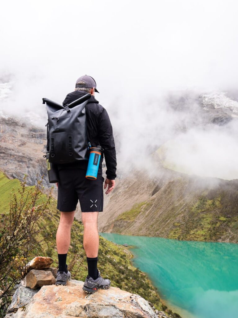 man with backpack and grayl water bottle looking at Humantay lake Peru